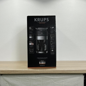 Die Verpackung der Krups KM8328 ist vollständig sichtbar und zeigt Abbildungen und technische Informationen auf der Seite.