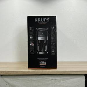 Die Verpackung der Krups KM8328 ist vollständig sichtbar und zeigt Abbildungen und technische Informationen auf der Seite.
