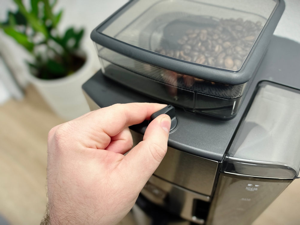 Ein Nutzer dreht am Aromaregler der Russell Hobbs Grind & Brew. Der Bohnenbehälter mit frischen Kaffeebohnen ist gut gefüllt.