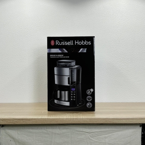 Die Vorderseite der Produktverpackung der Russell Hobbs Grind & Brew zeigt das Gerät und zentrale Funktionen. Das Design ist in Schwarz mit lila Akzent gehalten.
