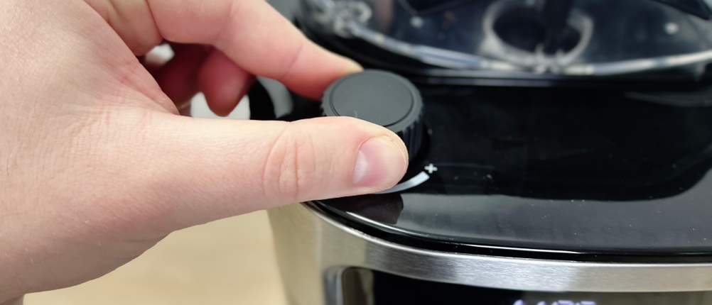 Ein Nutzer dreht am Aromaregler der Severin KA 4814, der sich seitlich am Bohnenbehälter befindet. Die Plus-Minus-Markierung ist sichtbar.