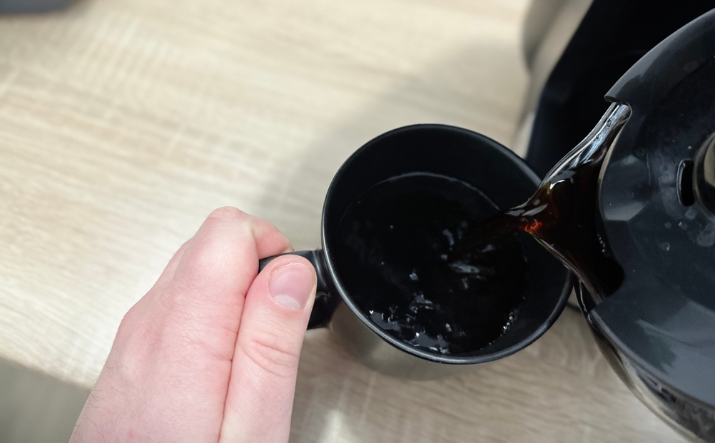 Frisch gebrühter Kaffee wird aus der Severin KA 4814 in eine schwarze Tasse gegossen. Die Hand hält die Glaskanne sicher.