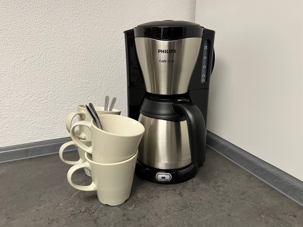 Kaffeemaschine mit Thermoskanne neben einem Stapel Tassen