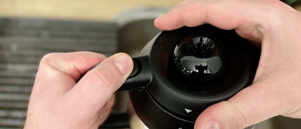 Zwei Hände öffnen den Verschluss der Rowenta CT3818 Thermoskanne. Der Fokus liegt auf dem Druckmechanismus am Griff der Kanne.