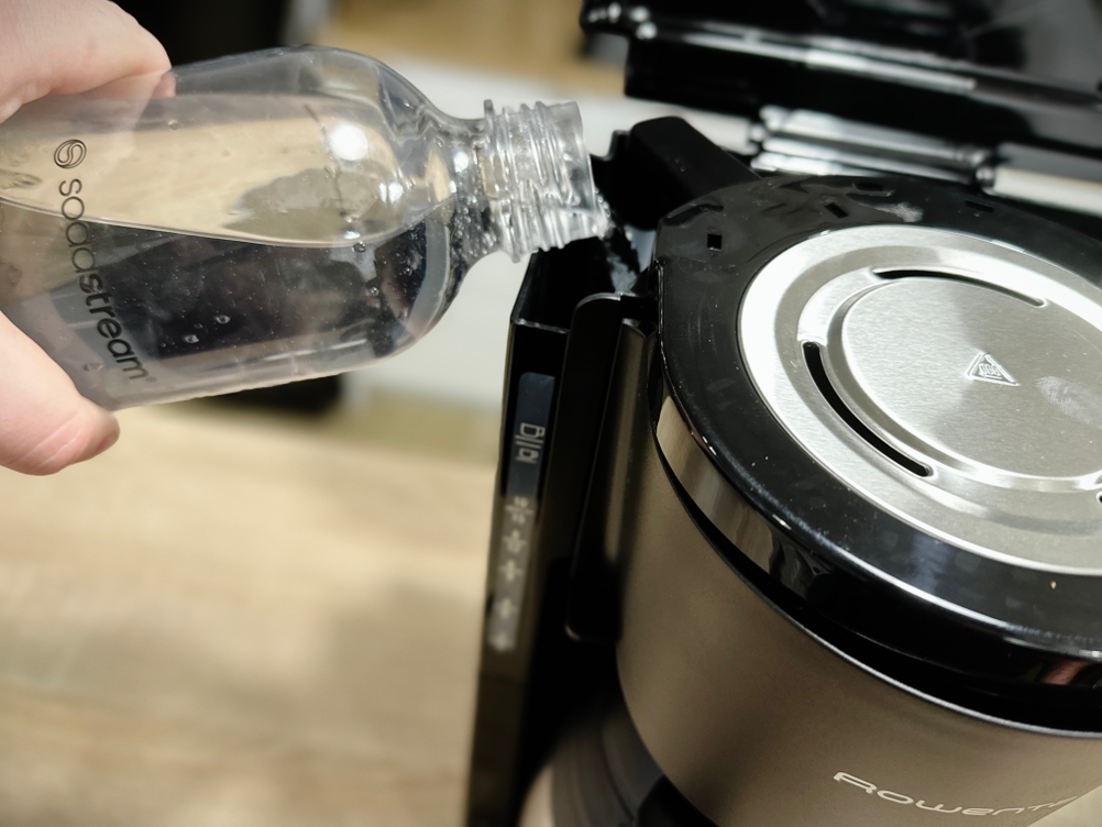 Wasser wird mit einer Flasche in den Wassertank der Rowenta CT3818 Kaffeemaschine eingefüllt. Der Filterdeckel ist geöffnet.