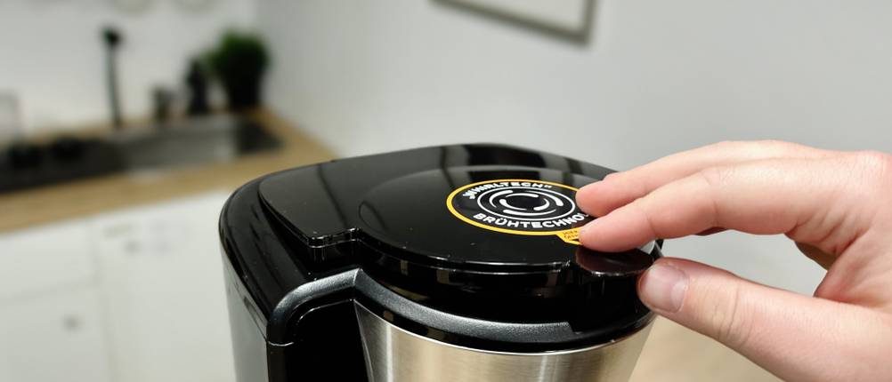 Die Hand eines Nutzers schließt den Deckel der Russell Hobbs Kaffeemaschine. Der Aufkleber zur WhirlTech-Brühtechnologie ist sichtbar.