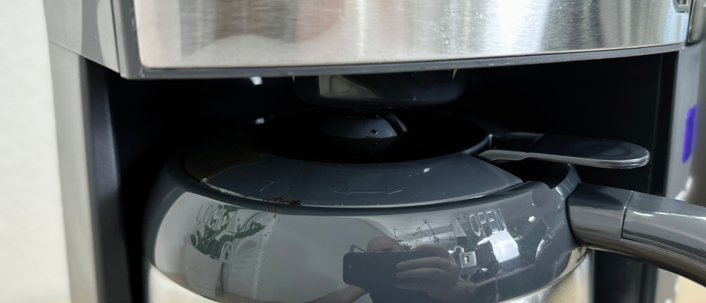 Kaffee läuft an der Kanne über und tropft auf das Edelstahlgehäuse der Maschine. Es ist ein kleiner Rückstand zu sehen.