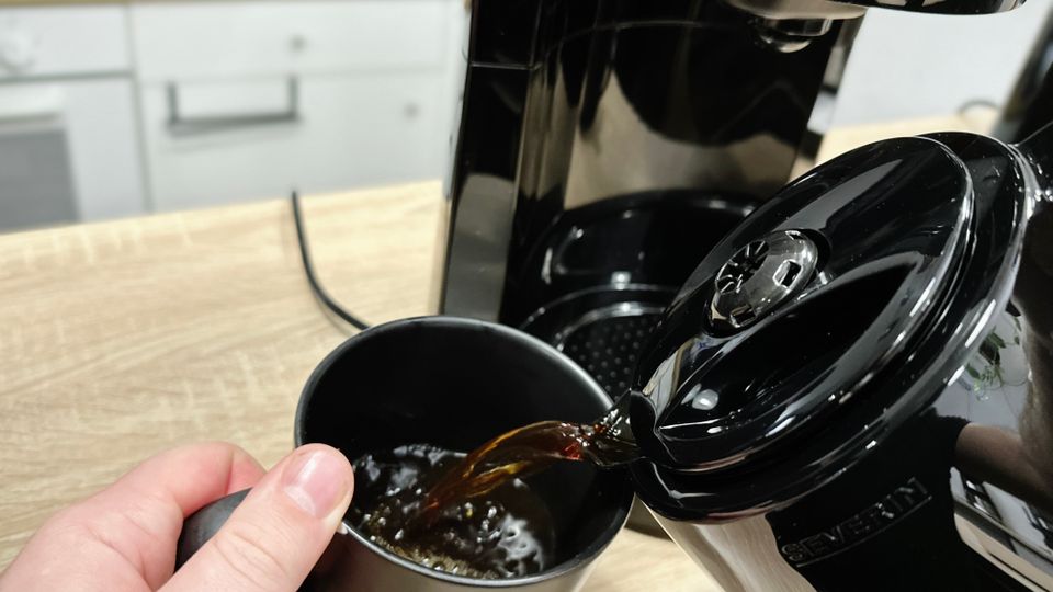 Kaffee wird aus der Severin KA 9250 Thermoskanne in eine schwarze Tasse eingeschenkt. Beide Hände halten Kanne und Tasse.