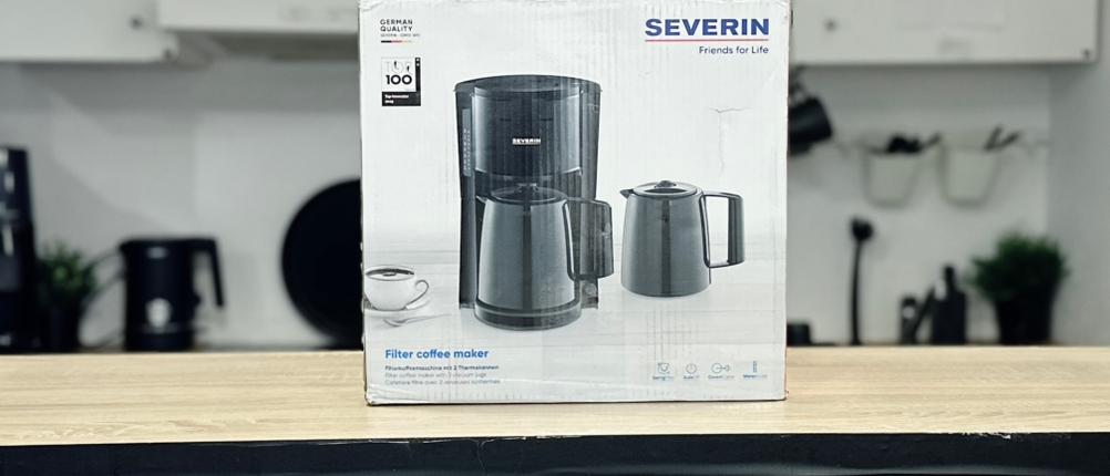 Verpackung der Severin KA 9250 mit Produktabbildung, zwei Thermoskannen und Tasse. Die Verpackung steht auf einer Holzfläche.