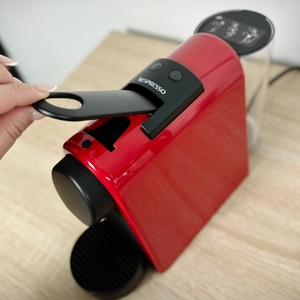 Eine Hand entnimmt das Kapselfach der Essenza Mini. Eine verbrauchte Kapsel ist sichtbar.