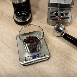 Auf einer Waage steht ein Behälter mit 12g Kaffeebohnen.