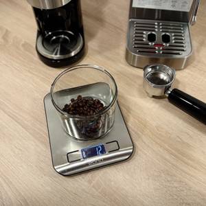 Auf einer Waage steht ein Behälter mit 12g Kaffeebohnen.