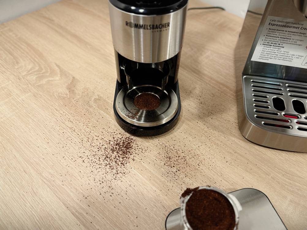 Neben der Kaffeemühle für Siebträger von Rommelsbacher liegt einiges an Kaffeepulver.