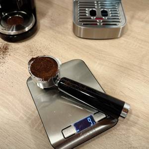 Eine Waage zeigt 9g an, darauf liegt ein mit Kaffeepulver gefüllter Siebträger.