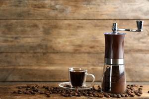 Timemore-Kaffeemühle-Test: Gefüllte Kaffeetasse steht neben Kaffeemühle inmitten von Kaffeebohnen.