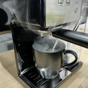 Aus der Breville Prima Latte II VCF108X strömt beim Milchaufschäumen deutlich sichtbarer Dampf in eine schwarze Tasse unter dem Auslauf.