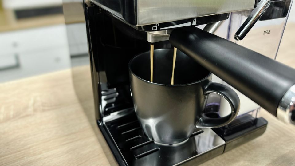 Kaffee läuft in zwei dünnen Strahlen aus dem Auslauf der Breville Prima Latte II VCF108X direkt in eine schwarze Tasse auf dem Abtropfgitter.