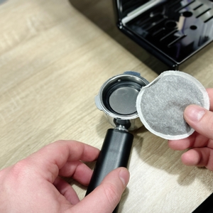 Ein Senseo-Pad wird in den geöffneten Siebträger der Breville Prima Latte II VCF108X gelegt. Die Maschine ist im Hintergrund sichtbar.