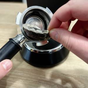 Ein benutztes Kaffeepad wird mit der Hand aus dem Siebträger der De'Longhi Dedica Style EC 685.B entfernt. Der Padträger ist noch feucht.
