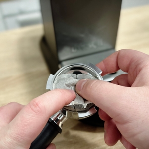 Ein Senseo-Pad wird von Hand in den Siebträger der De'Longhi Dedica Style EC 685.B eingelegt. Die Maschine steht im Hintergrund.