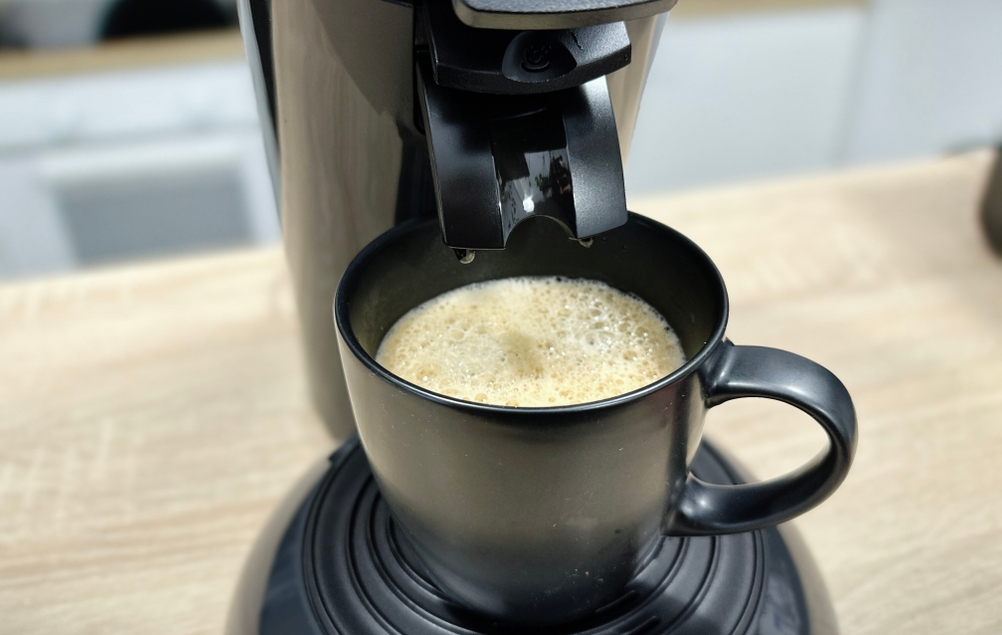 Kaffee mit feiner Crema ist frisch gebrüht in einer schwarzen Tasse unter der Philips Senseo HD6554/68 zu sehen.