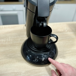 Ein Finger schaltet die Philips Senseo HD6554/68 über den zentralen Power-Knopf ein. Die Tasse steht bereits bereit.