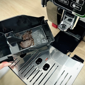 Die Abtropfschale des De'Longhi Dinamica (ECAM350.55.B) ist zur Entleerung geöffnet und zeigt frischen Kaffeesatz. Das Innenleben der Auffangschale ist klar strukturiert.