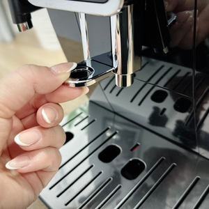 Eine Hand verstellt die Höhe des Kaffeeauslaufs der De'Longhi Dinamica (ECAM350.55.B). Der Auslauf lässt sich an verschiedene Tassengrößen anpassen.