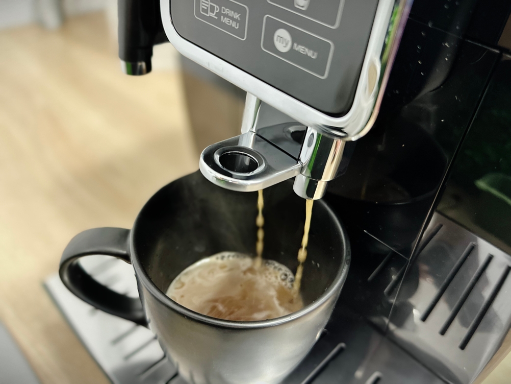 Der Kaffeevollautomat De'Longhi Dinamica (ECAM350.55.B) bereitet gerade einen Kaffee zu. Frisch gebrühter Kaffee läuft in eine Tasse.