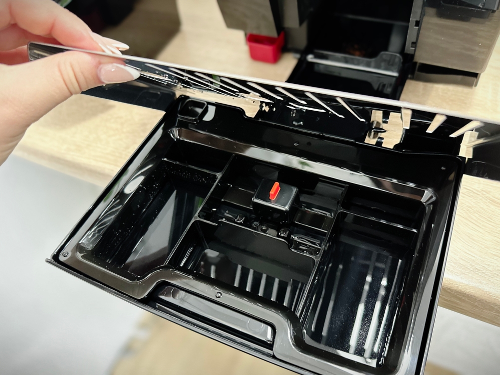 Die Wasserauffangschale des De'Longhi Dinamica (ECAM350.55.B) wird zur Reinigung geöffnet. Innen sind mehrere Kammern und ein roter Schwimmer zu sehen.