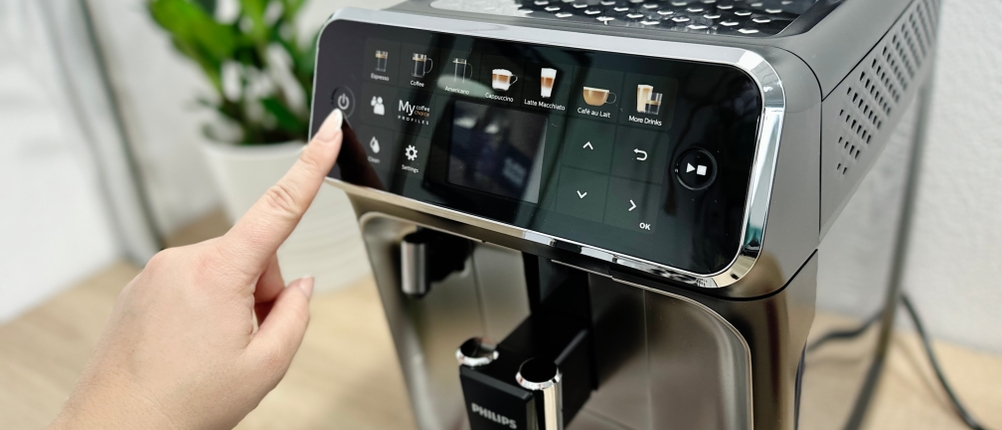 Eine Hand schaltet den Philips Series 5400 (EP5447/90) über das Touchpanel ein. Auf dem Display sind verschiedene Kaffeespezialitäten auswählbar.