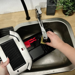 Eine Person reinigt die Auffangschale des Philips Series 5400 (EP5447/90) unter fließendem Wasser. Die Schale ist geöffnet.