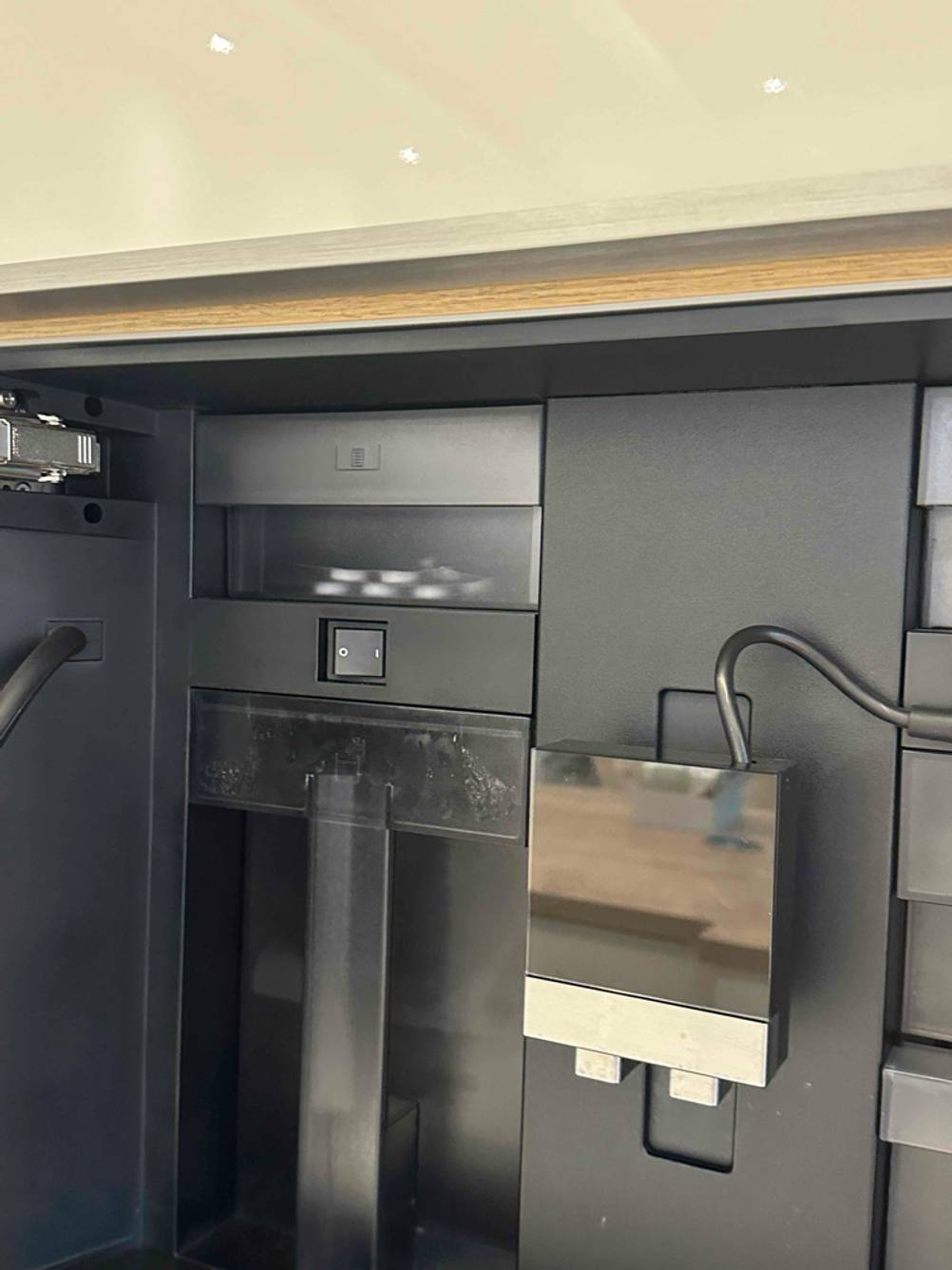 Einbau-Kaffeevollautomat im Test: Detailansicht des Inneren mit Powerknopf, Kabelzuführungen und Technik.