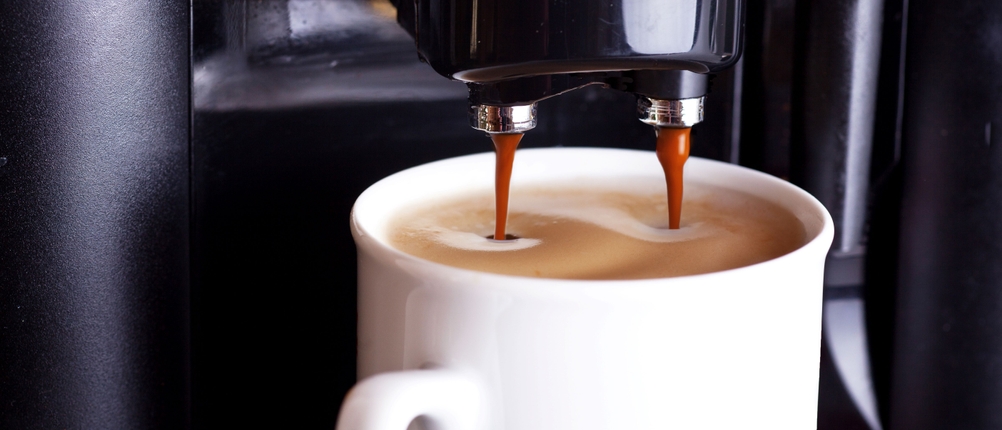 Kaffee fließt aus einem Kaffeevollautomaten in eine weiße Tasse.