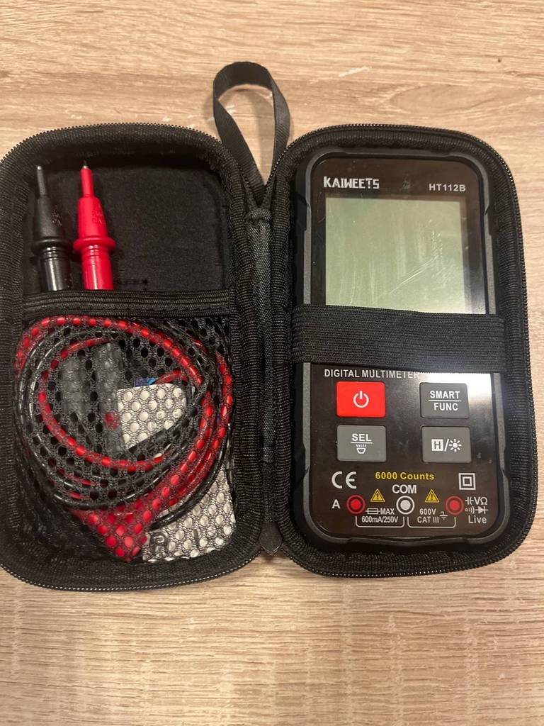 Schwarzer Kaiweets 112B digitaler Multimeter im Test liegt inklusive Aufbewahrungs-Etui auf beigefarbenem Untergrund.