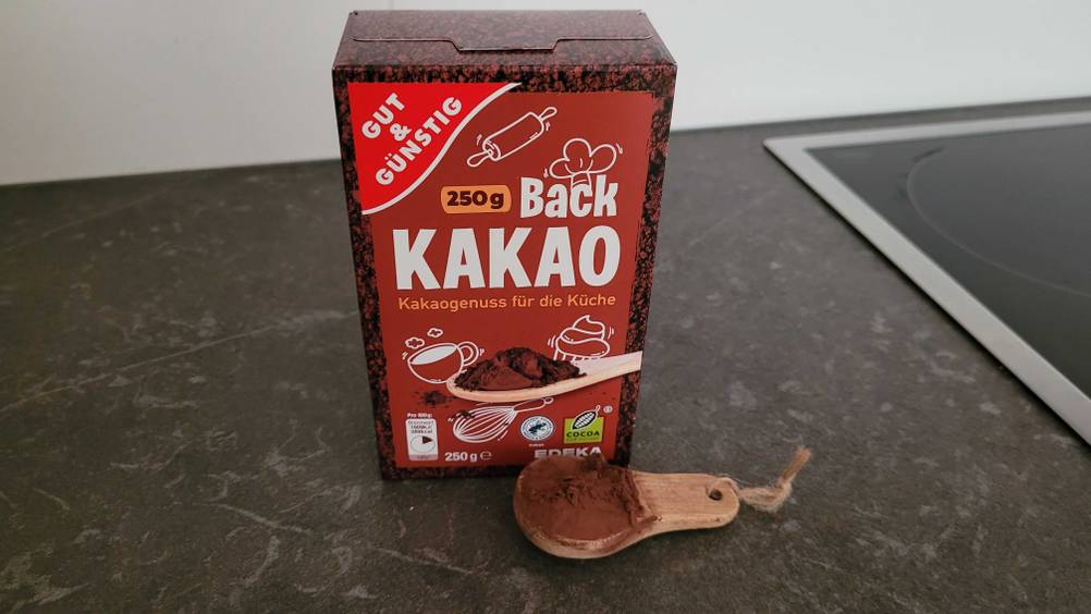 Kakaopulver getestet: Eine Packung auf einer dunklen Arbeitspaltte, davor einer Löffel mit Pulver.