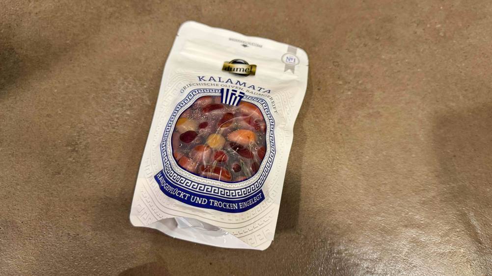 Kalamata-Oliven im Test: Eine Packung liegt auf einem beigen Boden.