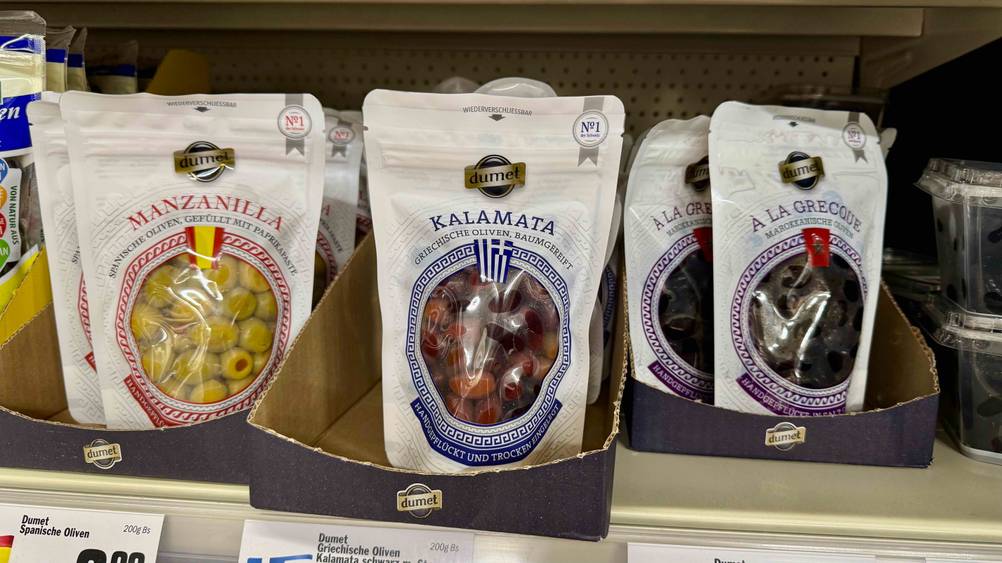 Mehrere Packungen der getesteten Kalamata-Oliven stehen in einem Regal neben anderen Produkten.