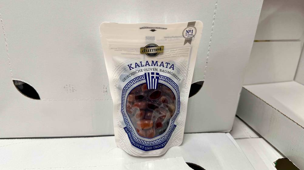 Kalamata-Oliven im Test: Eine Packung auf und vor hellen Kartons.
