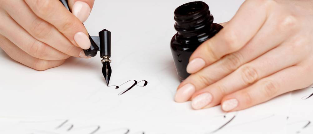 Kalligraphie-Set-Test: Hände halten Schreibfeder und Tintenglas.