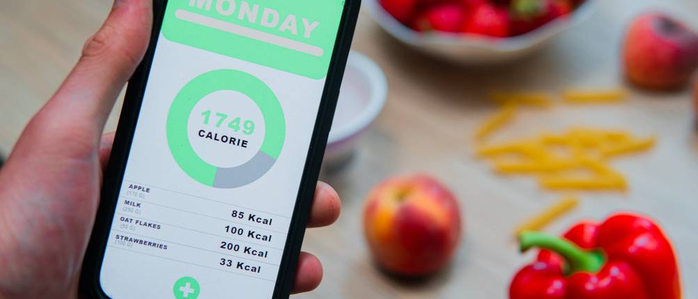Kalorienzähler-Apps im Test: Ein Smartphone wird über einem Tisch mit Gemüse festgehalten, während auf diesem eine Kalorienzähler-App geöffnet ist.