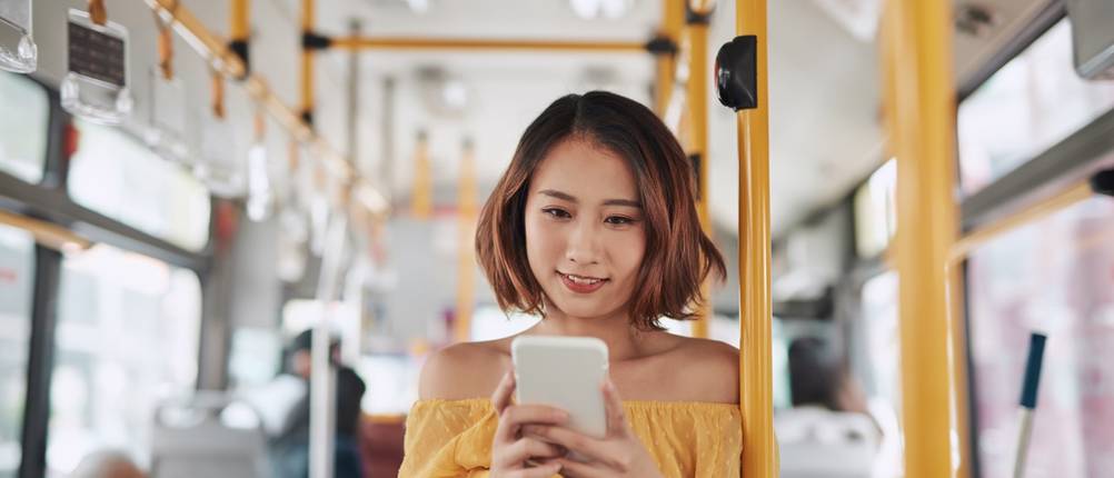 Junge Frau steht in einem Bus und schaut auf ihr Smartphone.