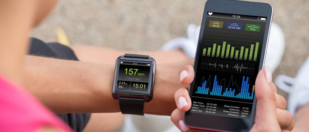 Smartwatch am Handgelenk zeigt 157 bpm, die andere Hand hält ein Smartphone mit Diagrammen.