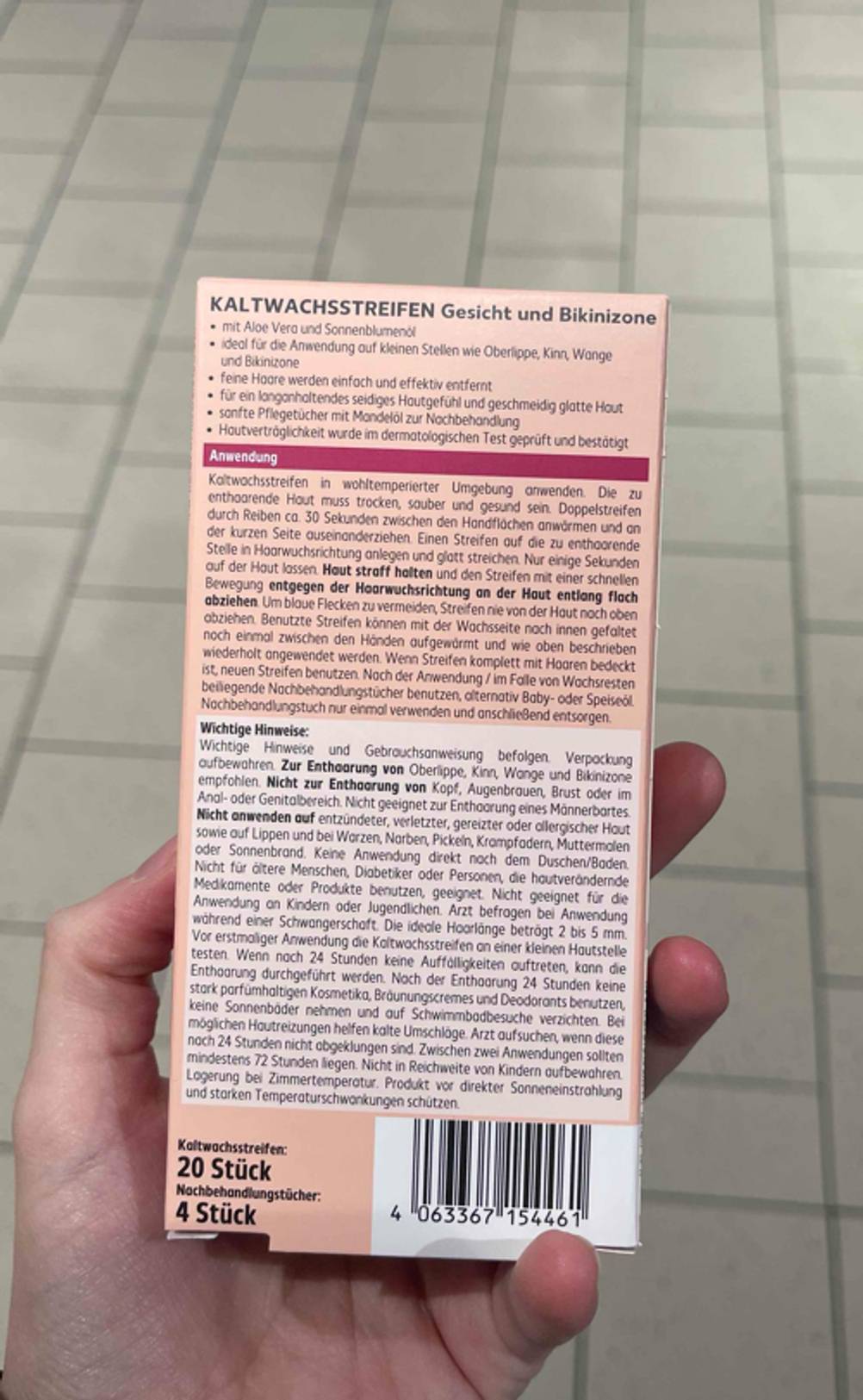 Die Rückseite der Verpackung der getesteten Kaltwachsstreifen Gesicht von einer Hand gehalten.