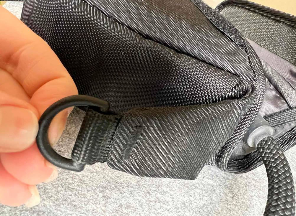 Nahaufnahme einer Plastikschlaufe der Kameratasche im Test von Fingern gehalten.