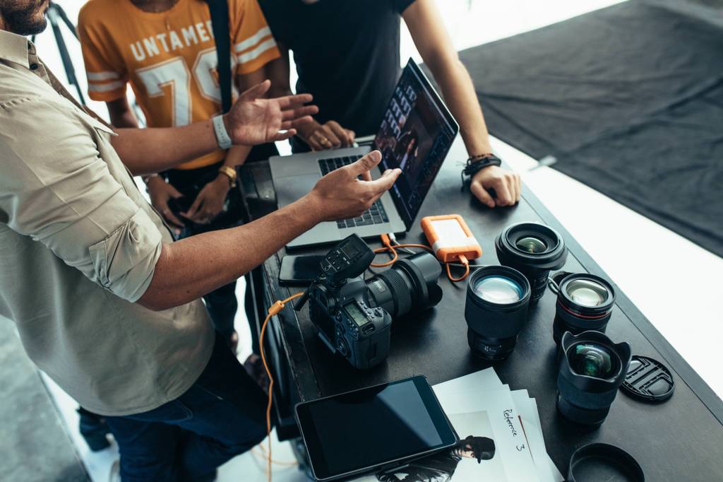 Ein Fotograf verbindet seine Kamera mit einem Laptop. Auf dem Tisch liegen mehrere Objektive.