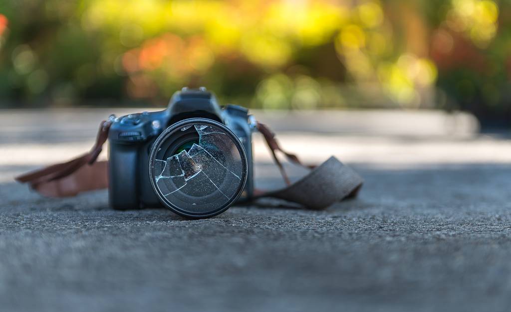 Eine Kamera mit zersprungenem Objektiv auf einem Steinboden.