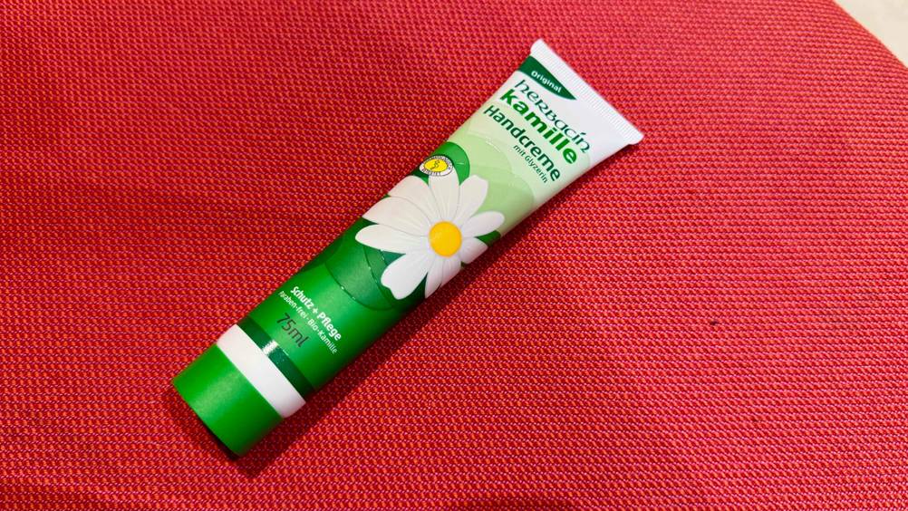Auf einer roten Fläche liegt eine Tube der Kamille-Handcreme im Test.