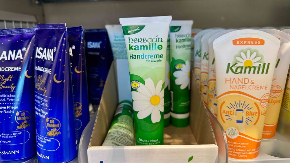 Mehrere Tuben Kamille-Handcreme in einem Verkaufsregal neben anderen Produkten.