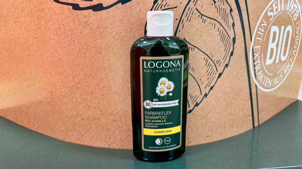 Kamille-Shampoo im Test: Eine Flasche von vorne vor einem Plakat.